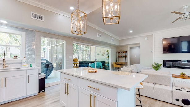 A modern kitchen with white cabinets and gold handles, a large island, and pendant lighting.