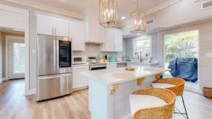 A modern kitchen with white cabinetry, stainless steel appliances, a central island with bar stools, and pendant lighting.
