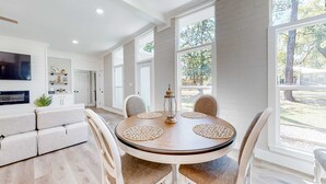 A modern kitchen with a dining area, large windows, and a flat-screen TV.