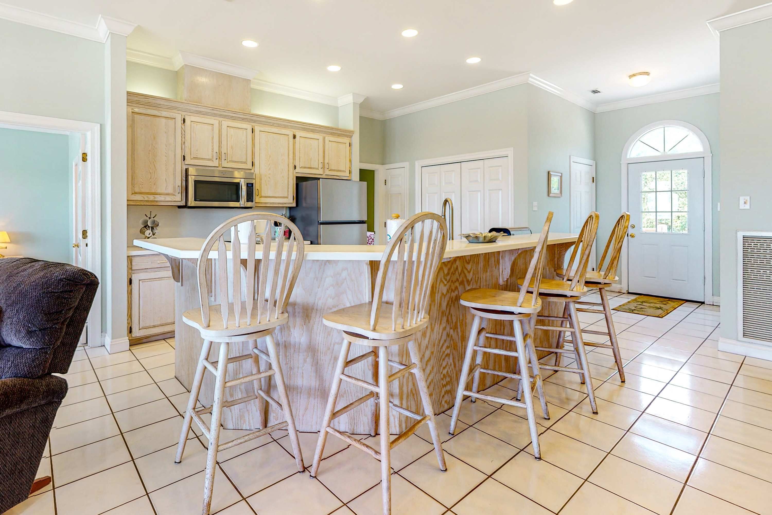 A kitchen with wooden cabinets, a stainless steel refrigerator, a microwave, and a dining area with four wooden chairs.