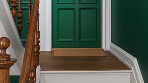 Una scala con ringhiere in legno che conduce a una porta verde con una fessura per la posta.