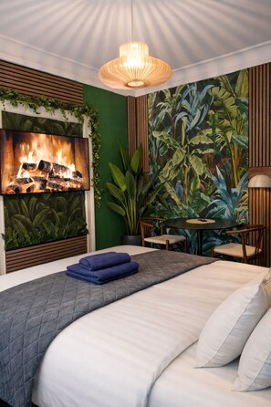 A bedroom with a bed, a wall-mounted TV, a table with chairs, and a large plant wall. - Greenbrook Homes - Jungle Suite (Aalborg)