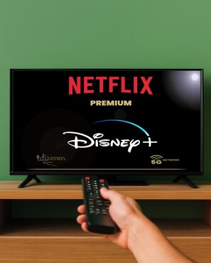 A television displaying the Netflix Premium Disney+ interface with a remote control in hand. - Greenbrook Homes - Jungle Suite (Aalborg)