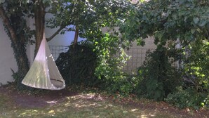 Un'area giardino con un'amaca sospesa, vegetazione fitta e un muro in mattoni sullo sfondo.