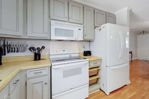 Una cocina con armarios blancos, microondas, estufa, refrigerador y encimera de madera.