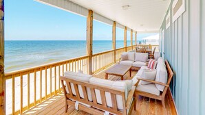 A covered deck with wooden furniture, a view of the ocean, and a railing. - Beautiful beach house with Gulf views, covered deck, central AC, and free WiFi (Dauphin Island)