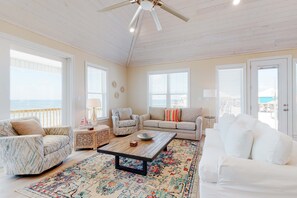 A spacious living room with a ceiling fan, large windows, and a view of the ocean.