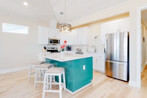 A modern kitchen with white cabinets, a stainless steel refrigerator, a central island with stools, and a hanging light fixture.