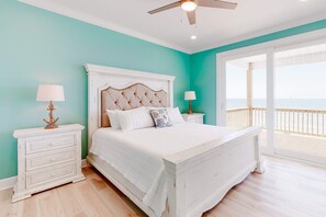 A bedroom with a bed, nightstands, and a view of the ocean.