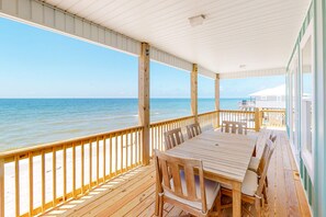 A covered outdoor deck with a wooden table and chairs, overlooking the ocean.