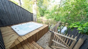 Une terrasse en bois avec un jacuzzi, entourée d’une clôture en bois et de verdure.