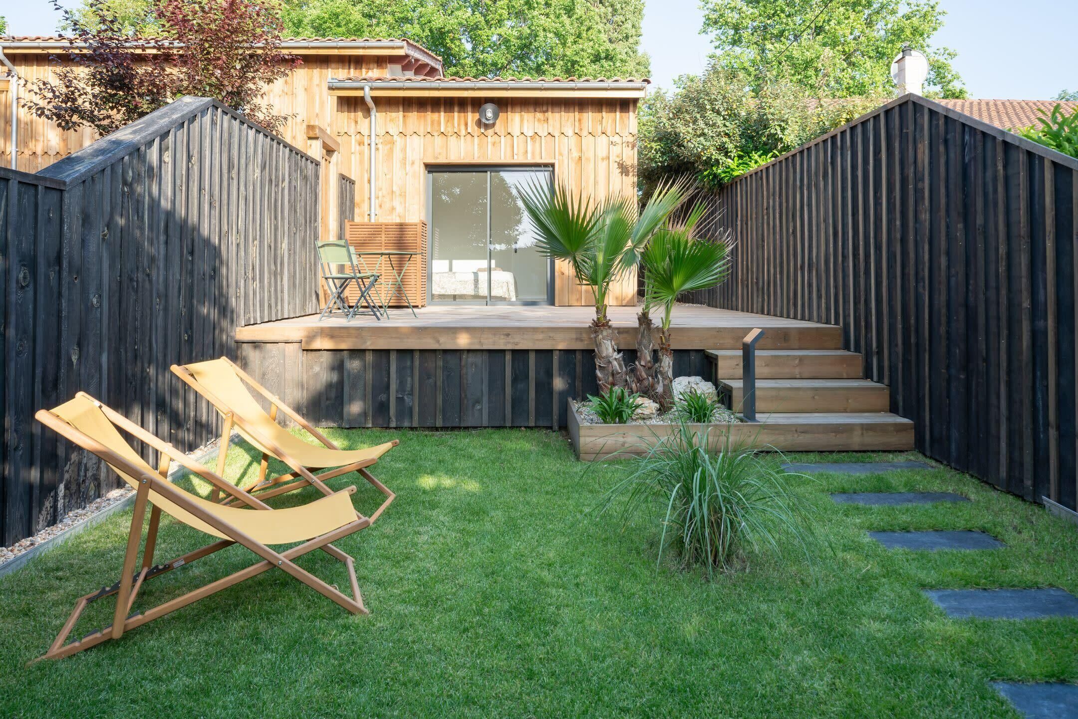 Un jardin avec une terrasse en bois, un petit espace patio avec une chaise et un jardin planté.