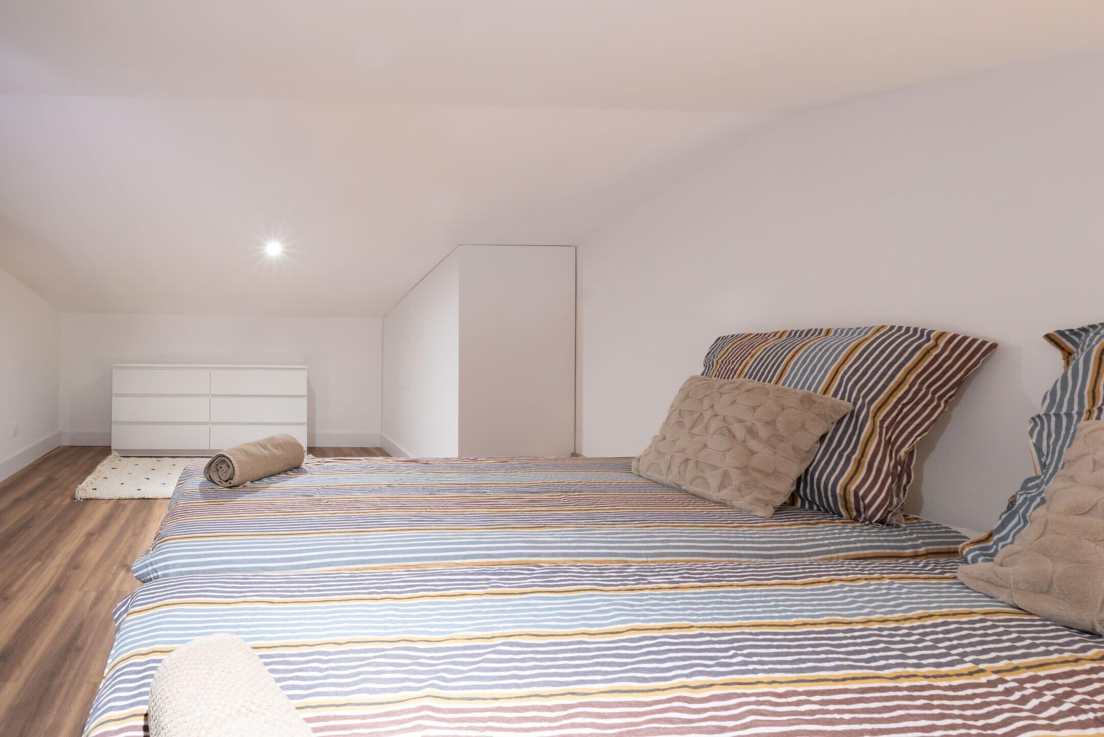 A bedroom with a striped bedspread, a white dresser, and a wooden floor.