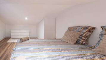 A bedroom with a striped bedspread, a white dresser, and a wooden floor.
