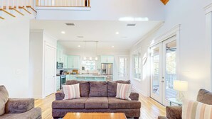 Ein Wohnzimmer mit braunem Sofa, Couchtisch aus Holz und Blick auf eine Küche und einen Balkon.