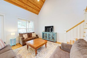 Un salon avec un plafond en bois, un téléviseur posé sur un meuble, un canapé, une table basse et un tapis à motifs.