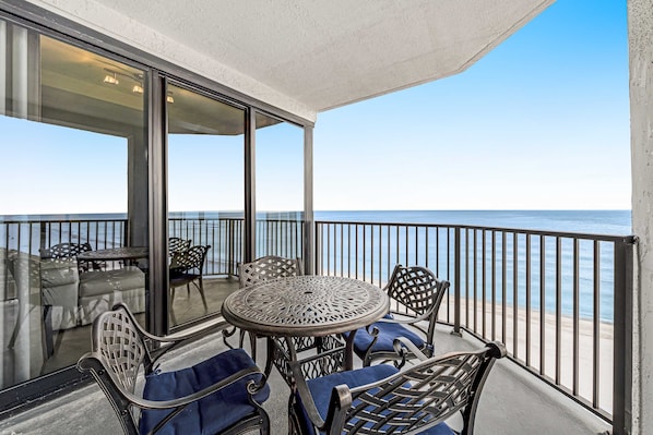 A balcony with a table and chairs, overlooking the sea. - Gulf-front 6th-floor condo with balcony, pool, hot tub, & sauna - beach access (Orange Beach)