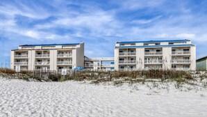 Un hotel sulla spiaggia con numerosi balconi, una spiaggia sabbiosa in primo piano e cieli sereni.