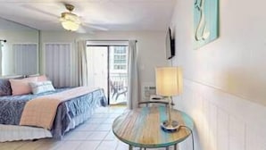 A hotel room with a bed, a small table with a lamp, a ceiling fan, and a view of the outside. - Updated studio w/shared outdoor pools and tennis court, family-friendly, & more! (Orange Beach)