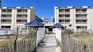 A pathway leading to a building with multiple balconies, a clear sky, and beach vegetation. - Updated studio w/shared outdoor pools and tennis court, family-friendly, & more! (Orange Beach)
