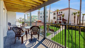 A covered outdoor area with a table and chairs, a view of buildings, and a well-maintained lawn. - Condo with partial Gulf views, shared outdoor pool, sun deck & private beach access (Orange Beach)