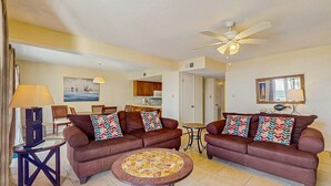 A living room with two brown sofas, a coffee table, a ceiling fan, and a dining area in the background. - Condo with partial Gulf views, shared outdoor pool, sun deck & private beach access (Orange Beach)