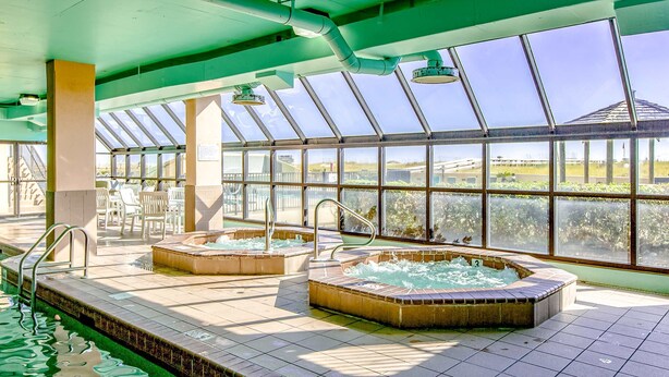 Una piscina interior amb dues banyeres d'hidromassatge, un sostre de vidre i vista a l'exterior.