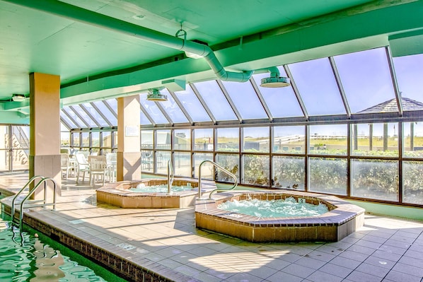 An indoor swimming pool with two hot tubs, a glass ceiling, and a view of the outdoors. - Ground floor, Gulf front condo with pools, hot tubs, tennis courts, and gym (Orange Beach)