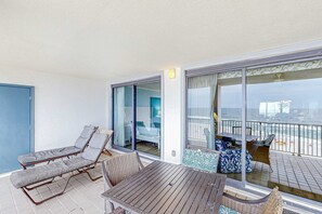 Varanda com mesa e duas cadeiras de apoio, vista para a praia, e porta de correr de vidro.
