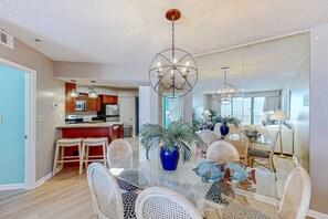 A dining area with a glass table, wicker chairs, a blue vase, and a chandelier. - Gulf front condo w unobstructed beach views - shared pools, hot tub, & tennis (Orange Beach)