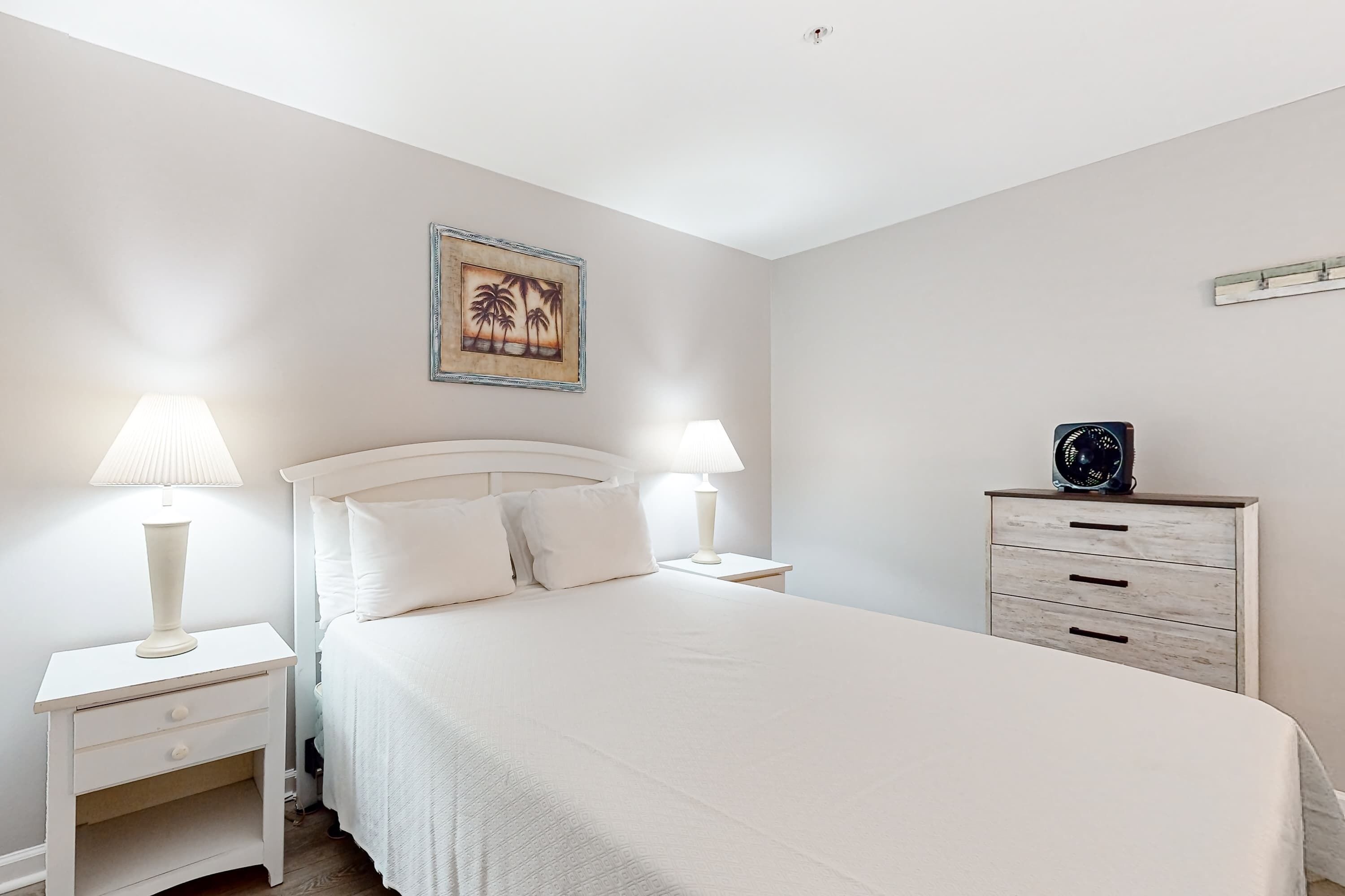Een slaapkamer met een bed, twee nachtkastjes met lampen, een nachtkastje, een dressoir en een wandklok.