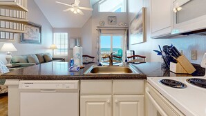 A kitchen with a dishwasher, stove, and sink. There is a ceiling fan, a window, and a door leading to a balcony. - Spacious condo near the beach with great view, bonus loft, and shared pool (Orange Beach)