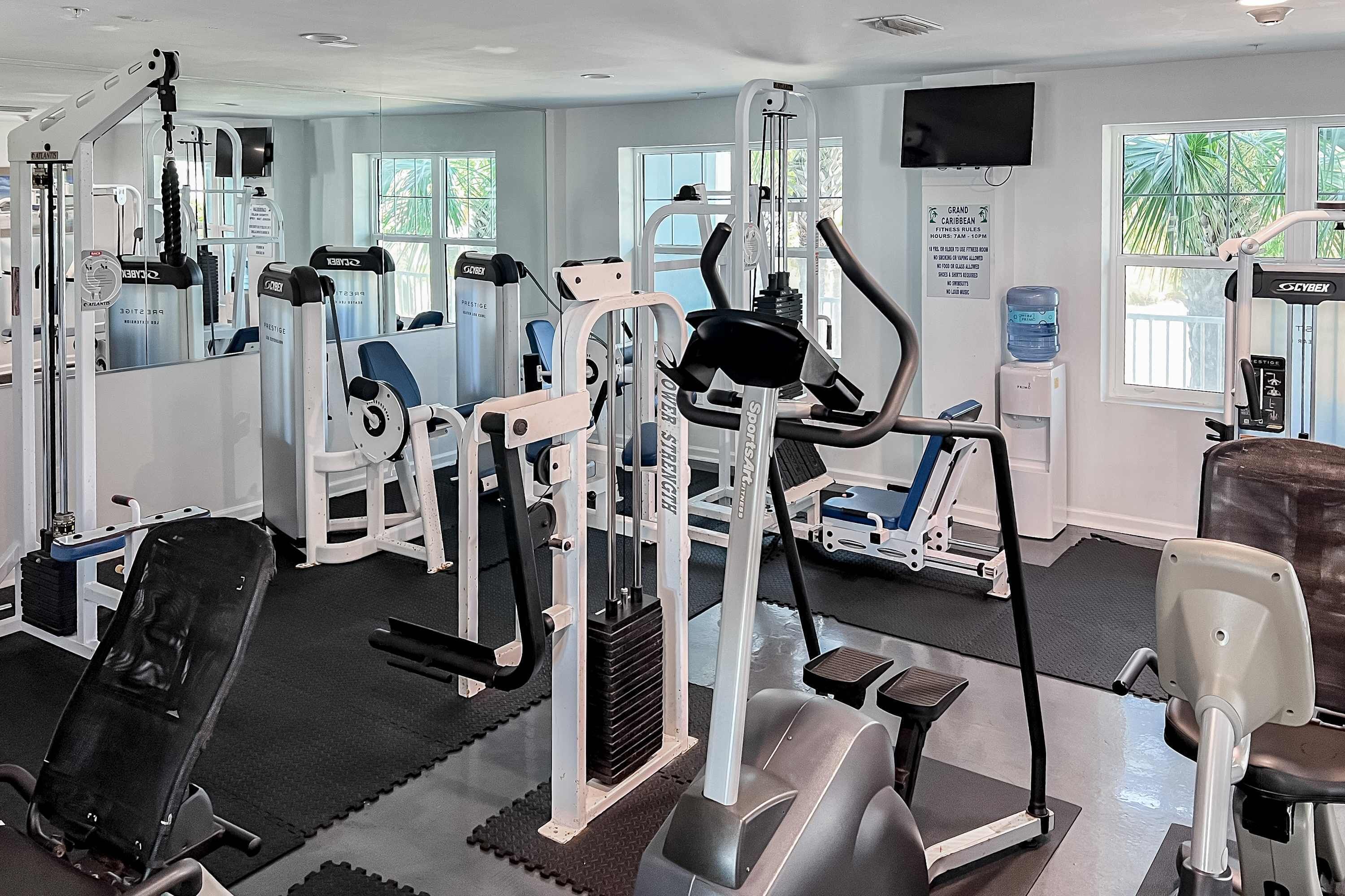 A gym with various exercise machines, a water dispenser, and a television on the wall.