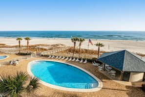 A pool with lounge chairs, a beach view, and a flag. - Inviting coastal-chic, beachfront condo with pool, hot tub, and tennis (Orange Beach)