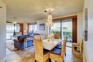 A modern living room with a dining area, a ceiling fan, and large windows. - Inviting coastal-chic, beachfront condo with pool, hot tub, and tennis (Orange Beach)