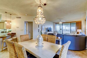 A dining area with a chandelier, wicker chairs, a dining table, and a kitchen in the background. - Inviting coastal-chic, beachfront condo with pool, hot tub, and tennis (Orange Beach)