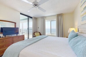 A hotel room with a bed, a television on a dresser, a chair, a window, and a ceiling fan. - Recently Updated Beachfront Condo w/ Incredible Views Plus Shared Pools, Hot Tub (Orange Beach)