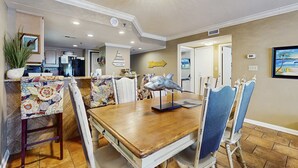 A dining area with a wooden table, patterned chairs, a fish sculpture, and a 'Come to Beach' sign. - Waterfront condo w/ a private balcony, community pools, & fitness center (Orange Beach)