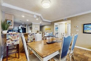 A dining area with a wooden table, patterned chairs, a fish sculpture, and a 'Come to Beach' sign. - Waterfront condo w/ a private balcony, community pools, & fitness center (Orange Beach)