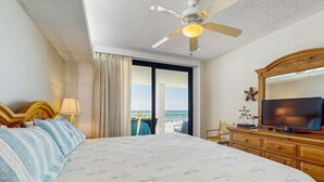 Habitación de hotel con cama, ventilador de techo, televisión, cómoda y balcón con vistas.