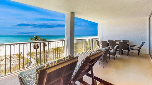 Un balcón con vistas a la playa y al océano, muebles de exterior y una mesa con sillas.