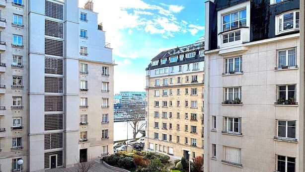 Un complesso residenziale con diversi edifici, un cortile centrale con vegetazione e una vista sul fiume sullo sfondo.