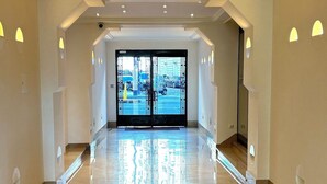 Un ampio e luminoso corridoio con pavimento riflettente che conduce a un ingresso con porta in vetro.