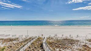 En strand med en træpromenade der fører ned til vandkanten, sandklitter og en klar blå himmel.