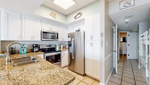 A modern kitchen with white cabinets, stainless steel appliances, and a granite countertop. - Coastal condo w/ shared, outdoor pool, indoor pool w/ hot tub, & relaxing sauna (Orange Beach)