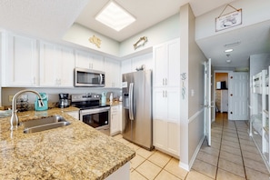 A modern kitchen with white cabinets, stainless steel appliances, and a granite countertop. - Coastal condo w/ shared, outdoor pool, indoor pool w/ hot tub, & relaxing sauna (Orange Beach)
