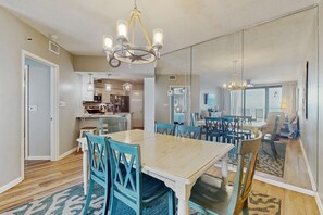A dining area with a large table and chairs, a chandelier, and a kitchen in the background. - Contemporary Gulf front condo w/ shared pools, hot tub, fitness center, beach (Orange Beach)