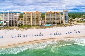 Ein Strandhotel mit mehreren Hochhäusern, einem Sandstrand mit blauen Liegestühlen und freiem Blick auf den Ozean.