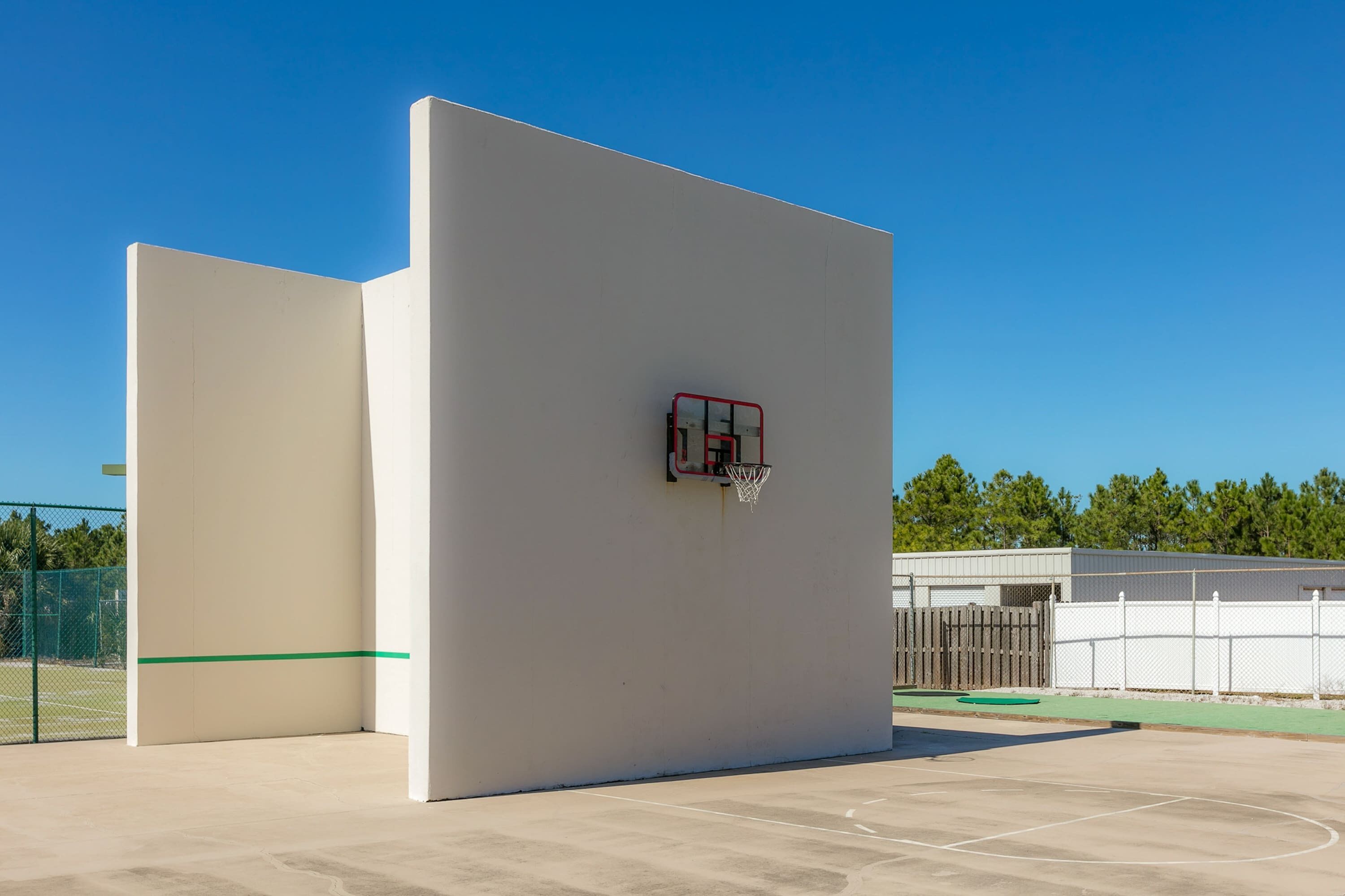 A basketball court with a hoop, a fence, and trees in the background.