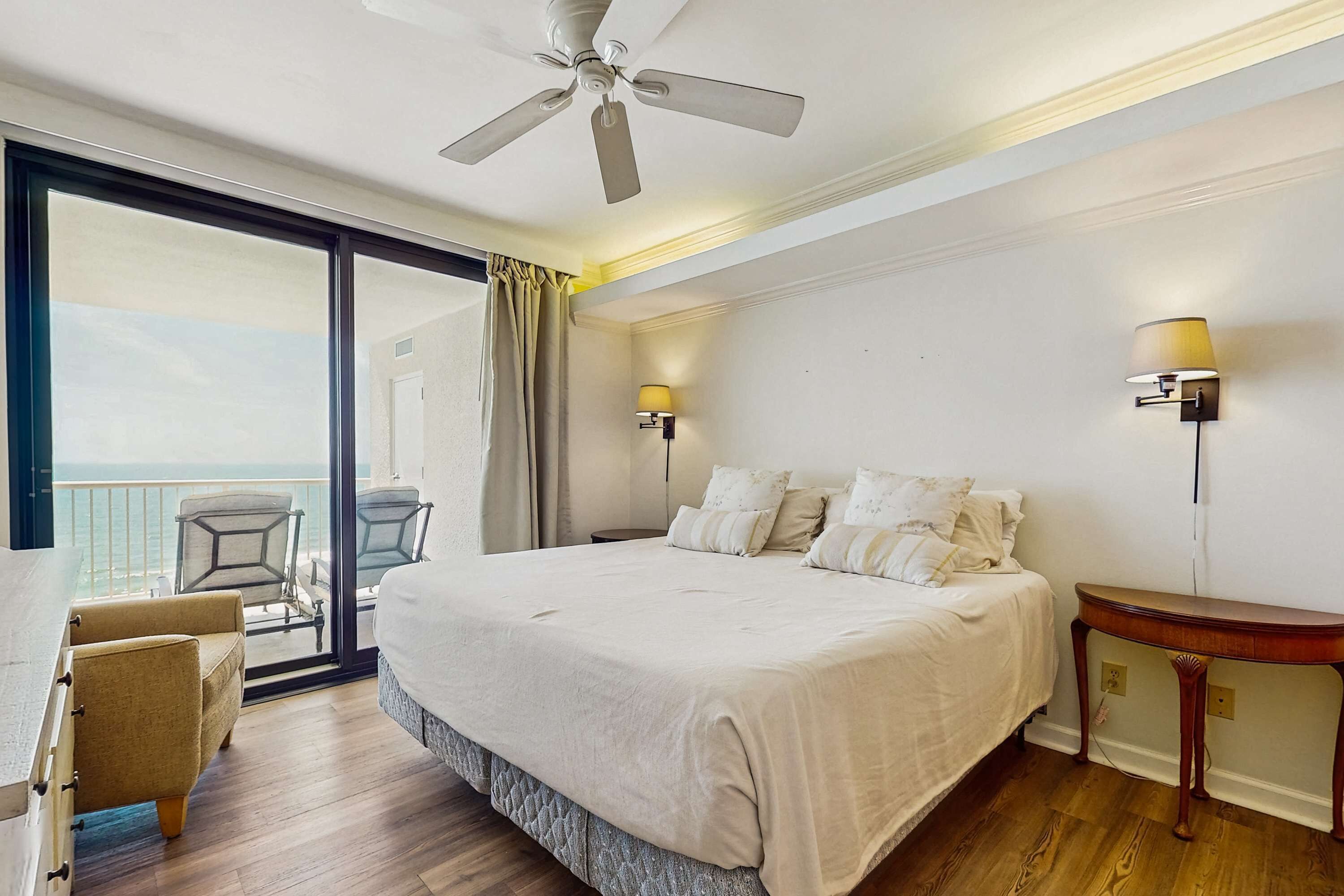 Habitación de hotel con cama, una silla, una mesa, ventilador de techo y vista al océano.